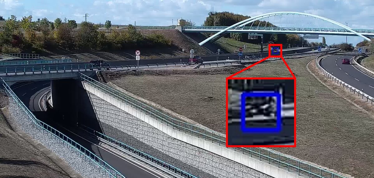 Small dark car stopped in shadow far from the traffic camera, detected and shown enlarged