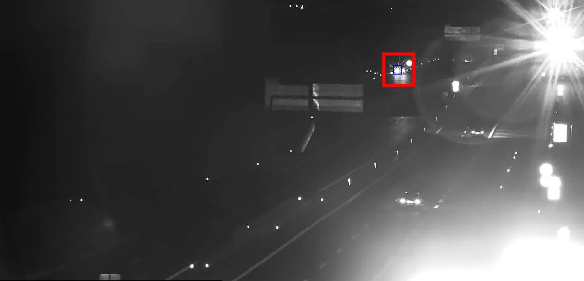 Distant stopped vehicle detected at night near a sign gantry